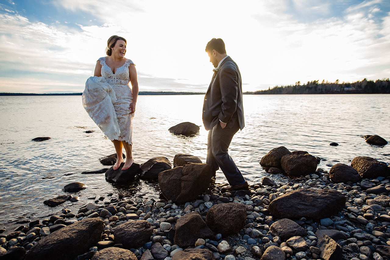 bride laughing at groom carefully walking out towards here on the seashore