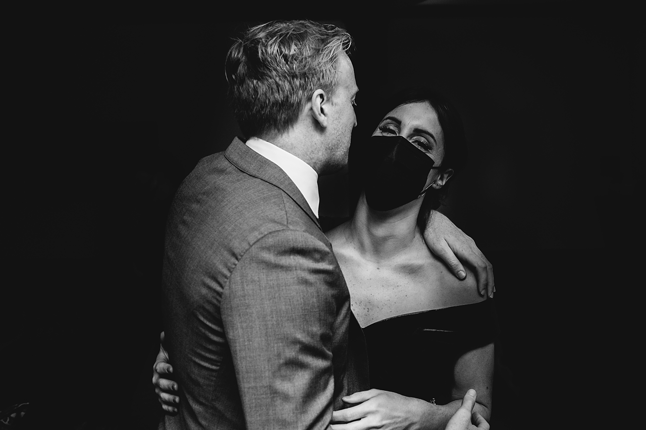 black and white photo of wedding guests in mask being embrace by her partner