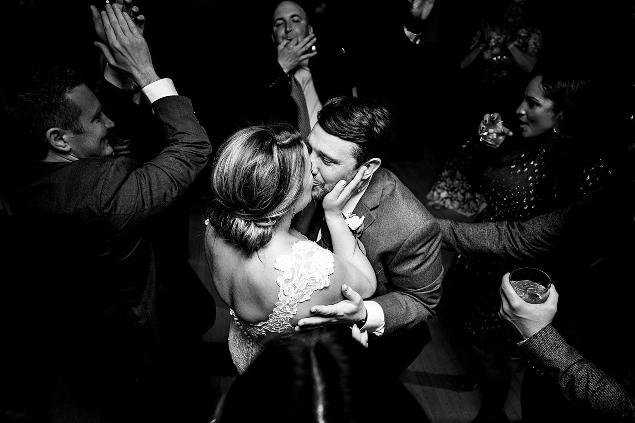 black and white photo of the wedding couple kissing amidst the dance party