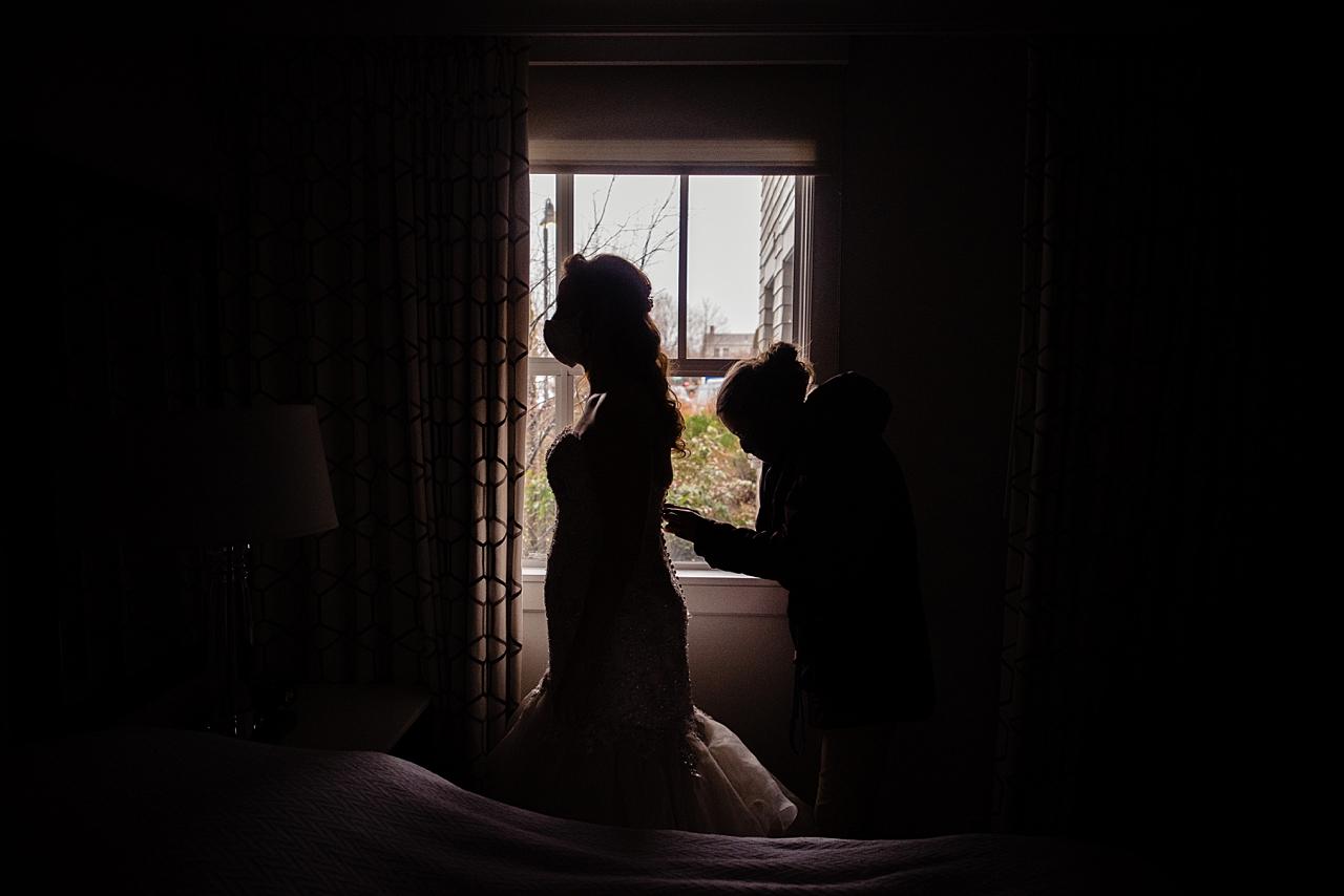 Bride getting zipped into her wedding dress by a window.